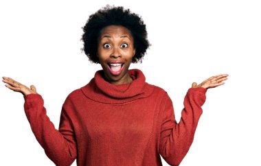 Afro saçlı, balıkçı yaka kazak giyen Afro-Amerikalı kadın zaferi mutlu bir gülümsemeyle ve ellerini kaldırarak kazanan ifadeyle kutluyor. 