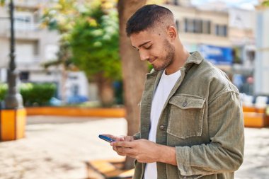 Parkta akıllı telefon kullanarak gülümseyen İspanyol genç adam.