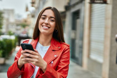 Genç İspanyol kadın şehirde akıllı telefon kullanarak mutlu bir şekilde gülümsüyor..