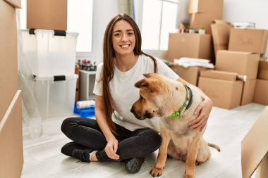 Genç İspanyol kadın gülümsüyor. Kendine güvenen, kucaklayan köpek yeni evinde yerde oturuyor.