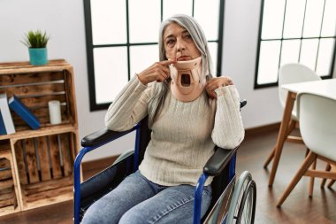 Orta yaşlı, gri saçlı, tekerlekli sandalyede oturan, tasmalı, ciddi yüzlü, eli çeneli, kafa karıştırıcı fikirleri olan bir kadın. 