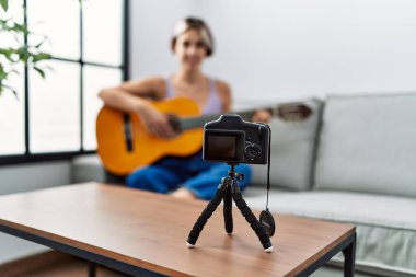 Beyaz bir kız evdeki koltukta kamerayla gitar konseri kaydediyor..