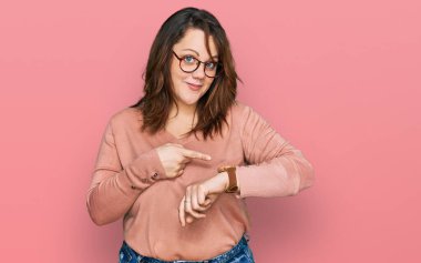 Gündelik kıyafet ve gözlük takan genç ve cüsseli bir kadın saati, sabırsızlığı ve gecikmeye kızmayı işaret ediyor. 