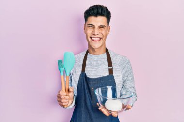 Ekmek hamuru tutan ve yemek pişiren genç İspanyol adam kameraya seksi bir ifadeyle bakıyor, neşeli ve mutlu bir yüzle.. 