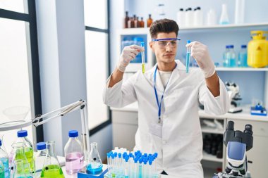 Laboratuvarda test tüpleri tutan bilim adamı üniforması giyen İspanyol bir genç.