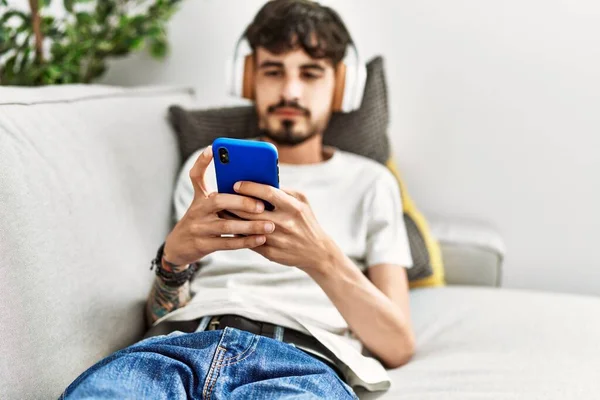 Jeune Homme Hispanique Utilisant Smartphone Écouteurs Couchés Sur Canapé Maison — Photo