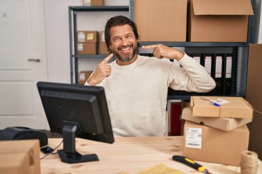 Küçük işletme şirketinde çalışan yakışıklı orta yaşlı bir adam neşeli bir şekilde gülümseyip parmaklarını ve ağzını işaret ediyor. diş sağlığı kavramı. 