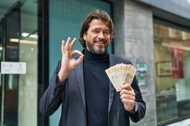 Yakışıklı orta yaşlı adam elinde 100 Danimarka kronu tutuyor. Parmaklarıyla imza atıyor, gülümsüyor. Mükemmel bir sembol. 