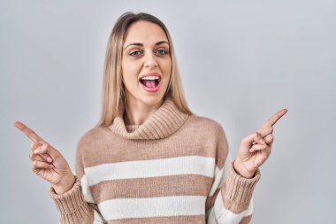 İzole edilmiş arka planda balıkçı yaka kazak giyen genç sarışın kadın farklı yönleri gösteren kendine güvenle gülümsüyor. reklam için kopyalama alanı 