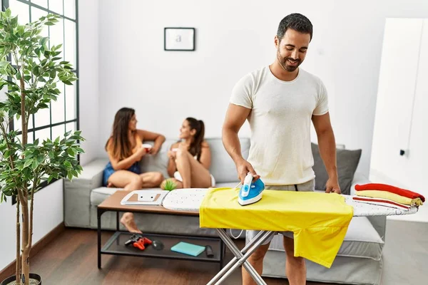 Kadınlar kanepede otururken, erkek gülümseyen mutlu ütü giysileri oturma odasında duruyor..