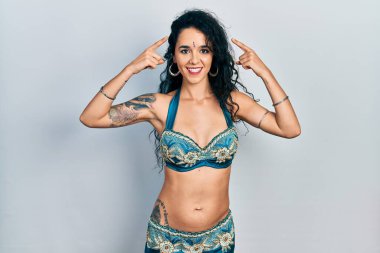 Bindi ve geleneksel dans kıyafetleri giyen genç bir kadın iki eliyle başını gösteren gülümseme, harika bir fikir ya da düşünce, iyi bir hafıza 