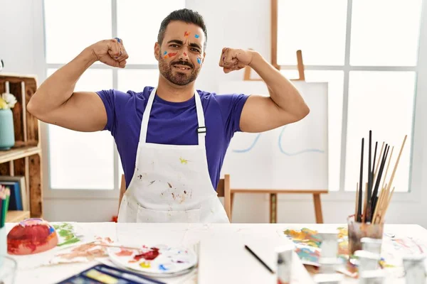 在艺术工作室里 年轻的有胡子的恐慌男子 脸上涂着彩绘 露出胳膊肌肉 带着自豪的笑容 健身概念 — 图库照片