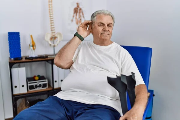 Homem Caucasiano Sênior Clínica Fisioterapia Segurando Muletas Sorrindo Com Mão — Fotografia de Stock