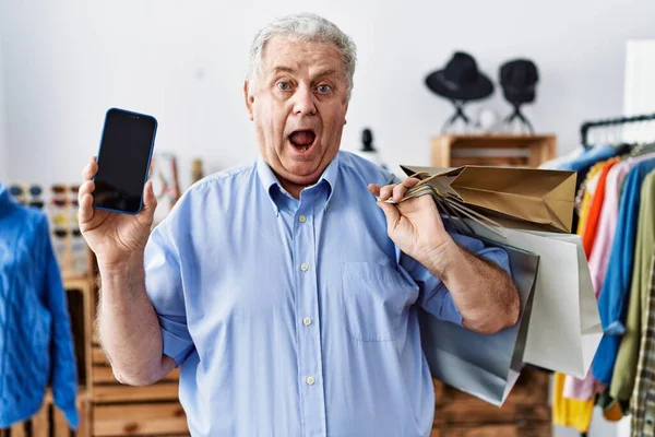Starší Muž Šedými Vlasy Drží Nákupní Tašky Ukazuje Obrazovku Smartphone — Stock fotografie