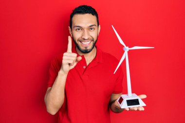 Sakallı İspanyol bir adam yenilenebilir elektrik için güneş değirmeni tutuyor. Bir fikir veya soru işareti ile gülümsüyor. 