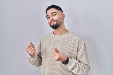 Soyutlanmış arka planda duran yakışıklı genç adam elleriyle para hareketi yapıyor, maaş istiyor, milyonerlik işi yapıyor. 