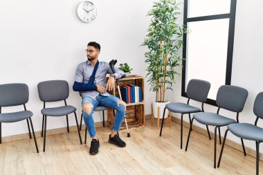 Koltukta oturan genç Arap adam klinik bekleme odasında koltuk değneği tutuyor.