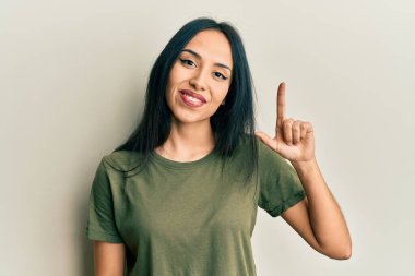 Gündelik tişört giyen genç İspanyol kız bir numarayı gösterip işaret ederken kendine güvenen ve mutlu bir şekilde gülümsüyor.. 