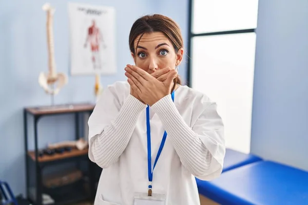 痛み回復クリニックで働く若いブルネットの女性は間違いのために手で口を覆いショックを受けました 秘密の概念 — ストック写真