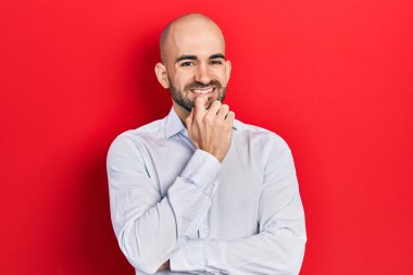 Zarif kıyafetler giymiş genç kel bir adam kameraya kollarını kavuşturup çenesine dokunarak gülümsüyor. Olumlu düşünmek. 