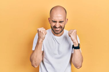 Başarı için heyecanlanan, kolları havada, gözleri kapalı, sıradan beyaz tişört giyen genç kel adam zaferi kutluyor. Kazanan konsept. 