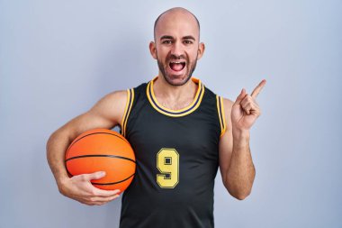 Sakallı, basketbol forması giyen, yüzünde kocaman bir gülümseme olan, eli kameraya bakan kel bir adam.. 