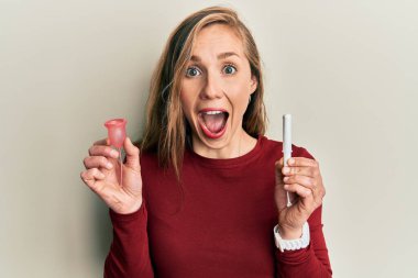 Genç sarışın kadın, elinde regl fincanı ve tampon tutarak kahkahalarla gülüyor.. 