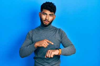 Balıkçı yaka kazak giyen sakallı bir Arap saati, sabırsızlığı ve gecikmeye öfkelenmeyi işaret ediyor. 