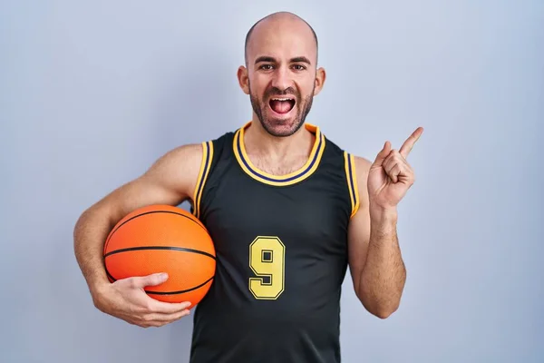 年轻的秃头男子 留着胡子 身穿篮球服 脸上挂着大大的笑容 手指头指向旁边看相机 — 图库照片