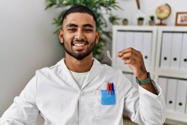 Dişçi kliniğinde çalışan genç Hintli adam elinde görünmez bir rakip tutuyor. Pozitif ve mutlu görünüyor. Kendine güvenen bir gülümsemeyle dişlerini gösteriyor. 