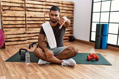 Spor salonundaki antrenman minderinde oturan genç Hintli adam mutsuz ve kızgın görünüyor. Reddedilmiş ve olumsuz. kötü ifade. 
