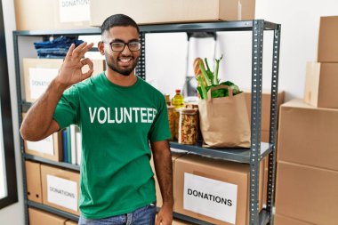 Genç Hintli gönüllü bağış kutusunu tutuyor gülümsüyor ve el ve parmaklarıyla tamam işareti yapıyor. başarılı ifade. 