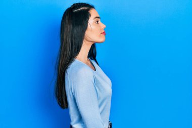 Latin kökenli genç bir kız günlük giysiler giyiyor. Yan tarafa bakıyor, rahat poz veriyor, kendine güvenen bir gülümsemeyle doğal bir yüz ifadesi sergiliyor.. 