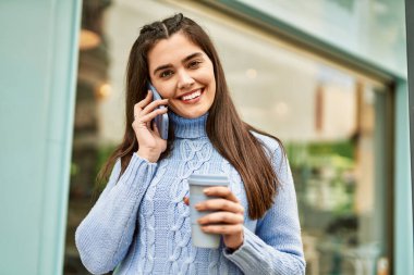 Genç İspanyol kız akıllı telefondan konuşuyor ve şehirde kahve içiyor.