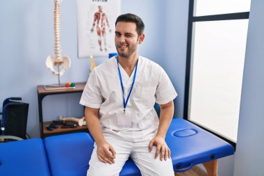 Sakallı, sakallı, acılı bir klinikte çalışan genç bir adam kameraya seksi bir ifadeyle bakıyor, neşeli ve mutlu bir yüzle.. 