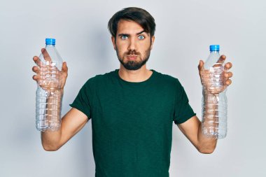 Genç İspanyol adam elinde plastik şişelerle komik suratlı yanakları şişiriyor. Ağzı havayla şişer, havayı yakalar.. 