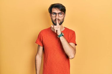 Gündelik kıyafetler ve gözlük takan genç İspanyol adam parmakları dudaklarında sessiz olmak istiyor. sessizlik ve gizli konsept. 