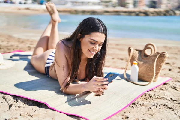 Young hispanic woman wearing bikini lying on sand at seaside