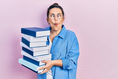 Genç İspanyol kadın gözlük takıyor ve kitap tutuyor. Ağzıyla balık suratı yapıyor ve şaşı bakıyor. Deli ve komik.. 