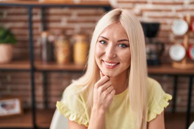 Evdeki masada dizüstü bilgisayar kullanan genç sarışın kadın.