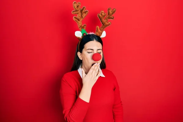 鹿のクリスマスの帽子と赤い鼻を身に着けている若いヒスパニック系の女性は手で口をカバー疲れあくび退屈 落ち着きもなく眠気もなく — ストック写真