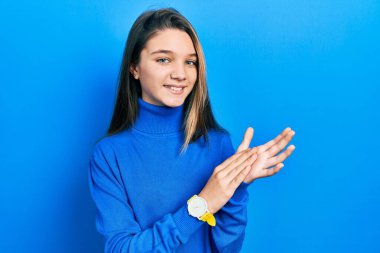 Balıkçı yaka kazak giyen genç esmer kız alkışlıyor ve mutlu ve neşeli, gururlu elleri alkışlıyor. 