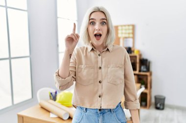 İnşaat ofisindeki genç ve güzel beyaz kadın başarılı bir fikirle işaret ediyor. Heyecanlı ve mutlu. Bir numara.. 