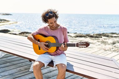 Genç İspanyol adam klasik gitar çalıyor sahilde bankta oturuyor..