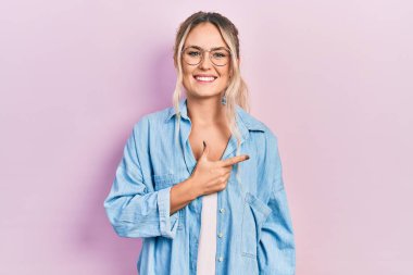 Güzel, genç, sarışın bir kadın. Günlük kıyafetler ve gözlük takıyor. Neşeli. Yüzünde mutlu ve doğal bir ifade var. 