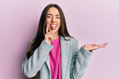 Young hispanic girl presenting with open palms, holding something sticking tongue out happy with funny expression. 