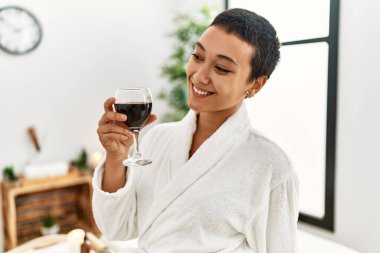 Genç İspanyol kadın bornoz giyip güzellik merkezinde şarap içiyor.
