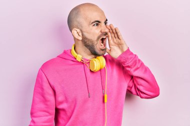 Spor kıyafetleri giyen, kulaklık takan, el ele verip bağıran genç kel bir adam. iletişim konsepti. 