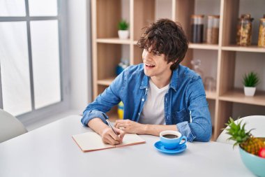 Genç İspanyol adam evde ders çalışırken deftere yazıyor.