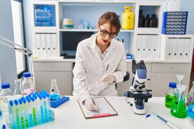 Laboratuvarda elinde deney tüpü tutan bilim adamı üniforması giyen beyaz bir kadın.